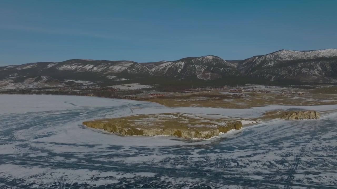 Ilmakuvaa saaresta ja Baikaljärven jäätyneestä rantaviivasta halkeilevine jääkuvioineen, lumikenttineen ja vuorijonoineen talvella, Venäjällä.