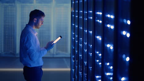 it technician in data center digital server room controlling work of rack server cabinets with a tablet. professional server engineer at work.