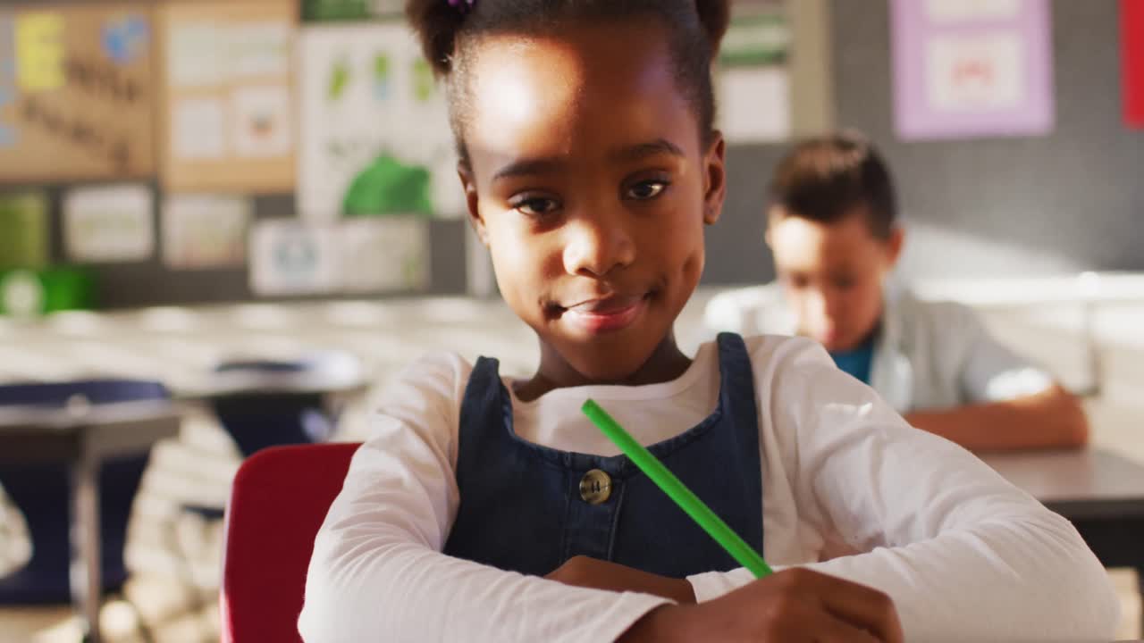 Portrait of african american schoolgirl sitting in class, making notes, looking at camera