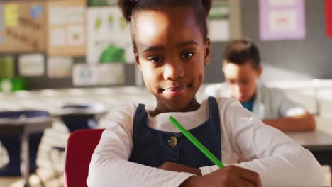 portrait of african american schoolgirl sitting in class, making notes, looking at camera