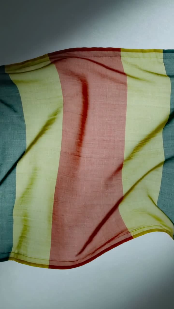 Video verticale: Sciarpa a righe appesa, la piega superiore che ondeggia verso il basso, un angolo che si solleva, sistemandosi per la moda.