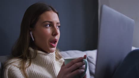 mujer bebiendo café mientras tiene un chat de video en su computadora portátil en casa