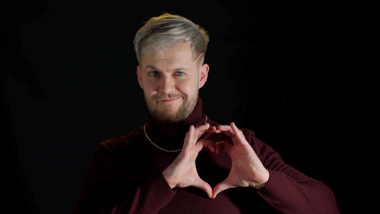 hombre elegante sonriente con ojos azules mostrando forma corazón con manos señal en forma de corazón, bondad humana
