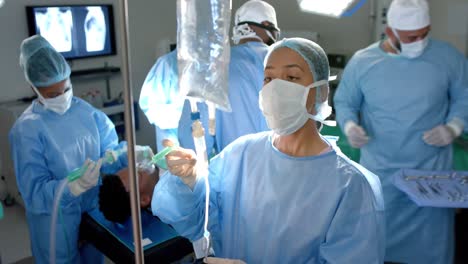 Diverse-surgeons-wearing-surgical-gowns,-applying-drip-in-operating-theatre,-slow-motion