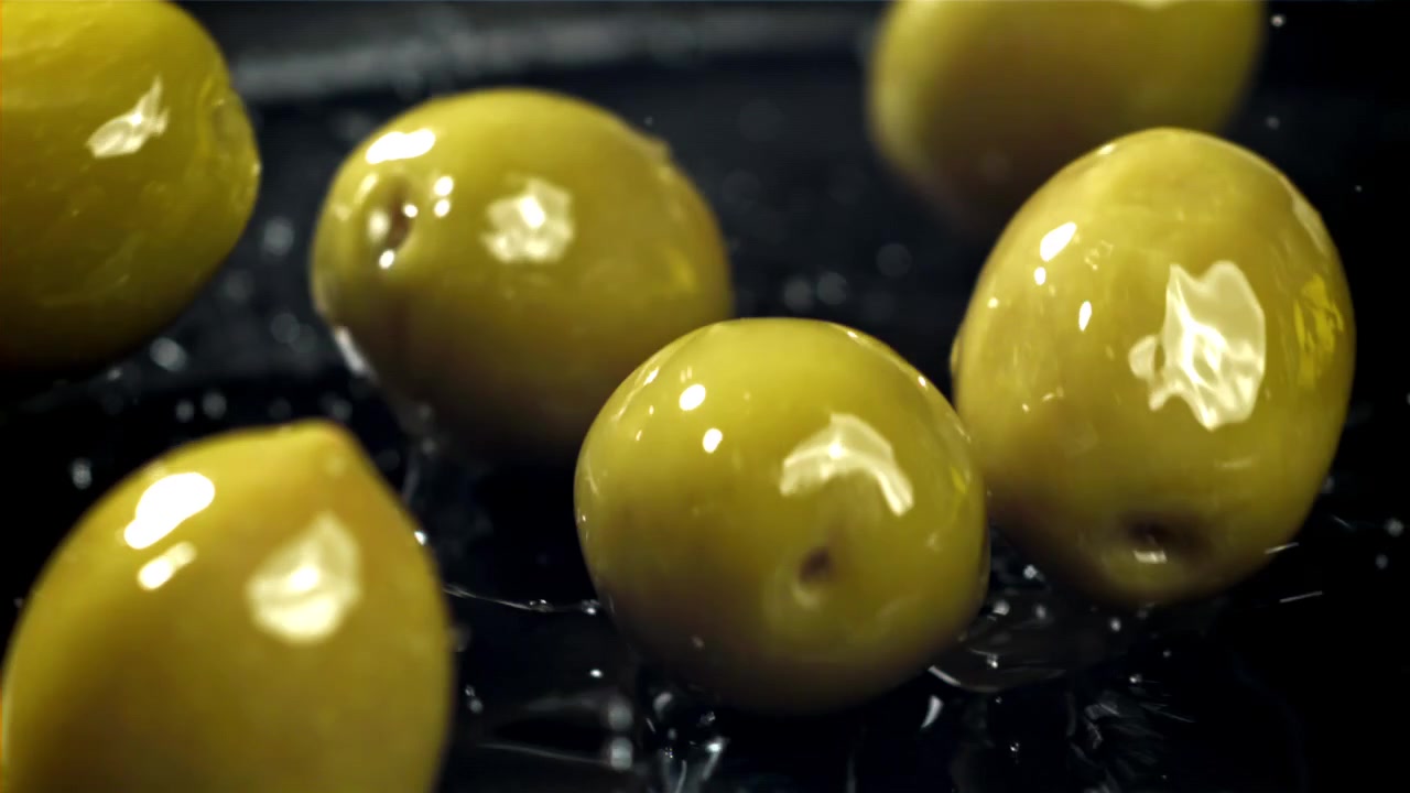 Olive verdi che cadono e schizzano acqua su una superficie scura al rallentatore