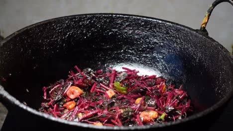 cooking a stir-fry with reddish-purple leaves and shrimp in a cast iron pan