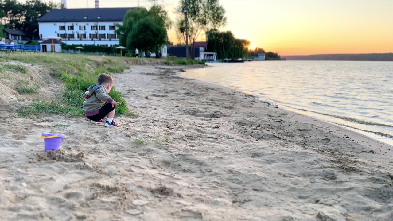 Little toddler boy sitting on the beach playing peacefully in the sand. Kid drops a shovel and takes sand with bare hands.