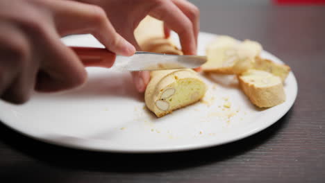 in a home kitchen a hand cuts cantucci biscuits before second baking in oven