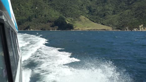 Schaumige-Wellen,-Die-Auf-Der-Seite-Des-Kreuzfahrtschiffes-In-Marlborough-Sounds,-Neuseeland,-Mit-Grünen-Hügeln-Im-Hintergrund-Brechen