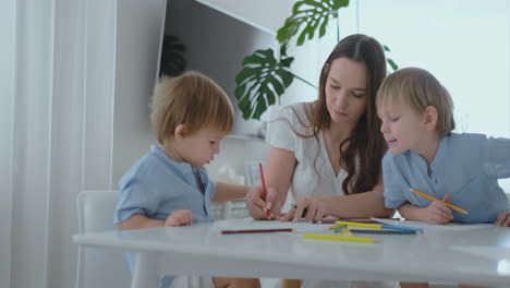 Young-Mom-and-two-sons-2-4-years-old-draw-pencils-drawing-on-boomega-sitting-at-the-living-room-table-in-slow-motion