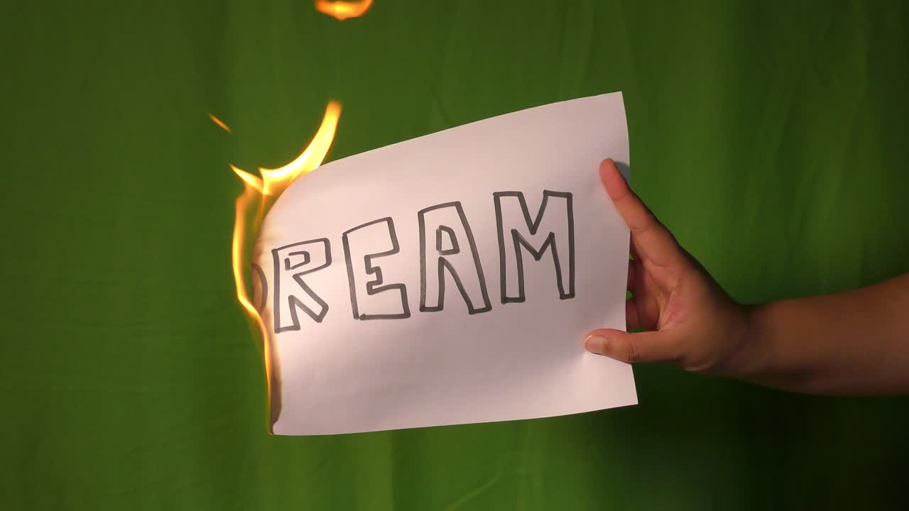 한 손은 꿈의 텍스트 단어가 새겨진 불타는 종이를 들고 있습니다.