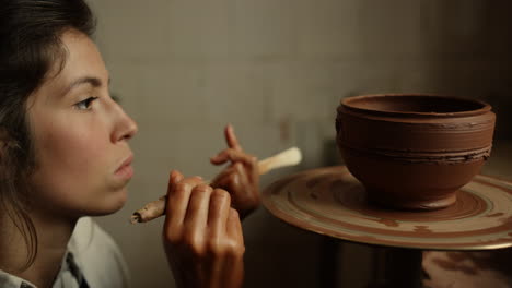 focused artist making handicraft in pottery. girl scraping ornament in workshop