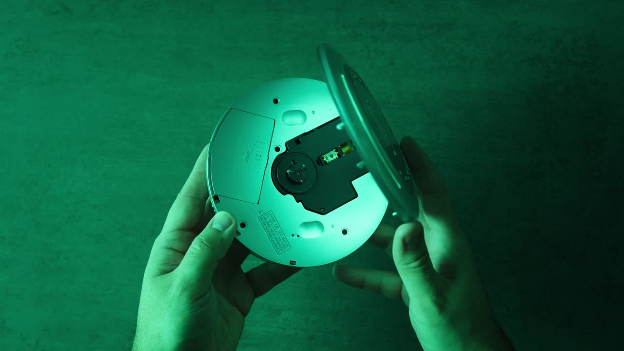 초록색 빛 아래에 열린 휴대용 cd 플레이어를 들고 있는 손