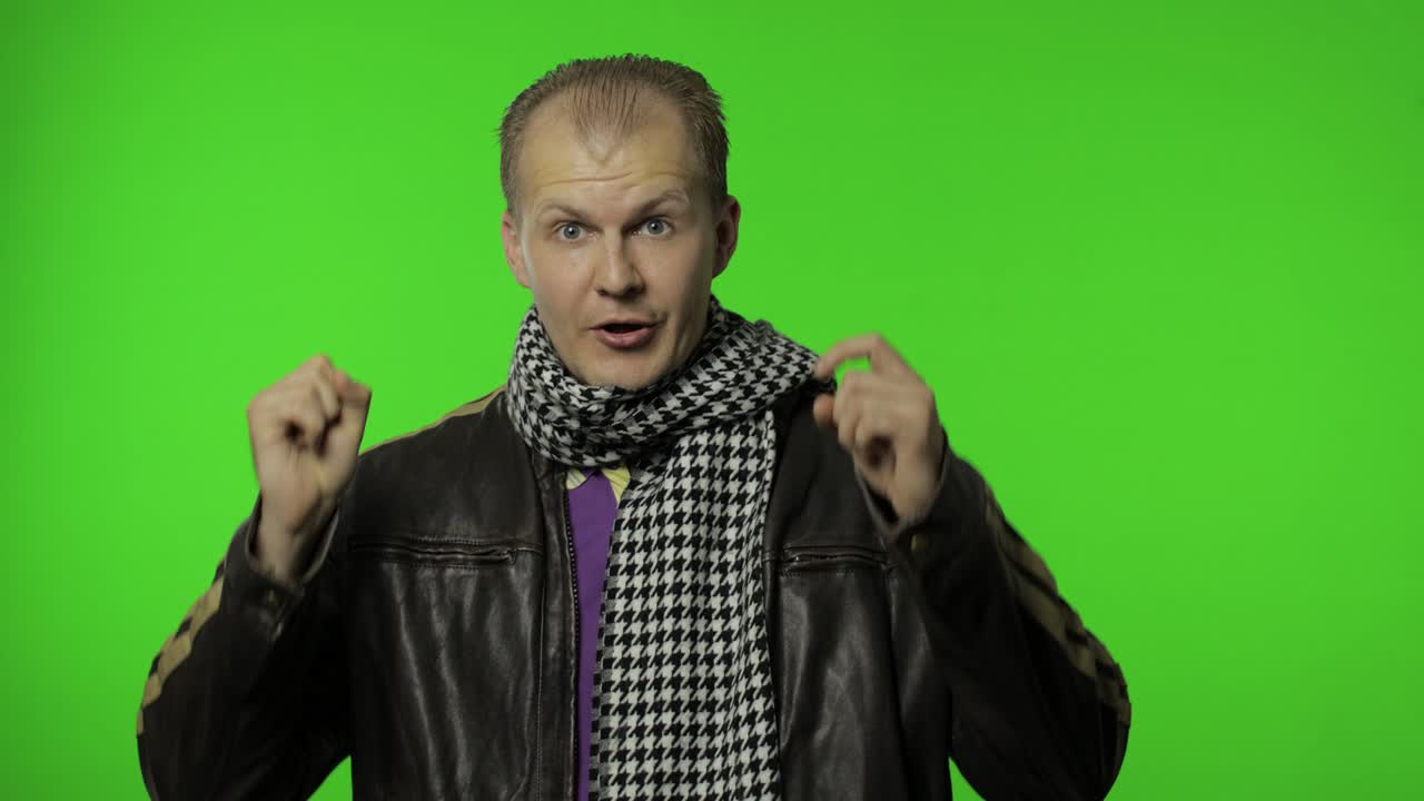 hombre de rock positivo y guapo en chaqueta de vaqueros marrón señalando con el dedo a la cámara.