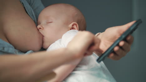 close up of woman using mobile phone while breast feeding newborn baby