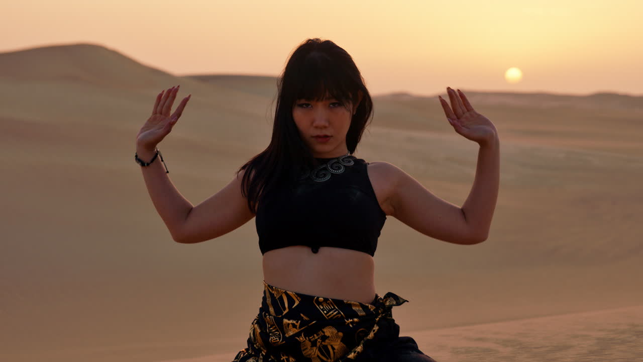 사하라 사막 에서 해가 지는 동안 모래 언덕 을 배경 으로 모래 를 던지는 여자