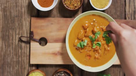 Video-of-hands-of-caucasian-woman-adding-parsley-to-curry-in-bowl-on-wooden-surface