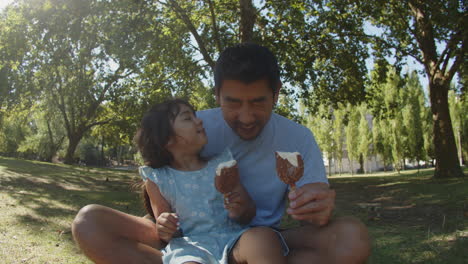 retrato de feliz padre asiático y su hija comiendo helados de chocolate en el parque