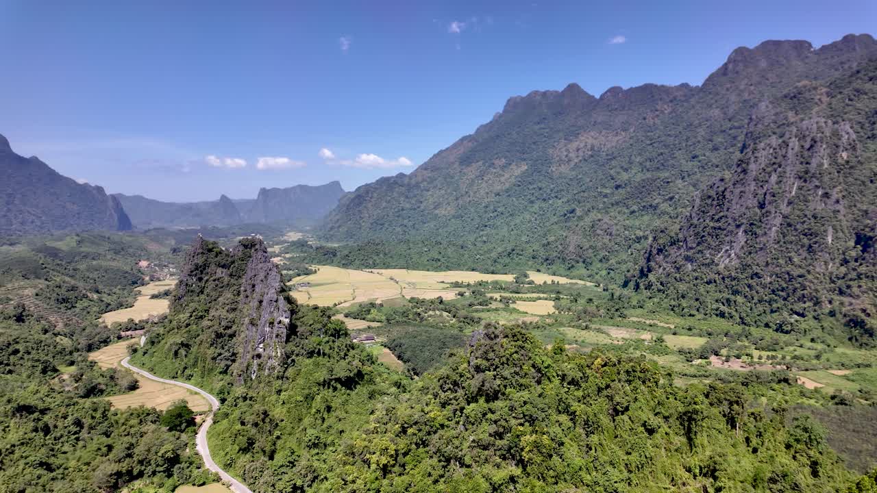Paesaggio panoramico del Laos con campi, aspre montagne calcaree e una strada tortuosa attraverso una valle lussureggiante