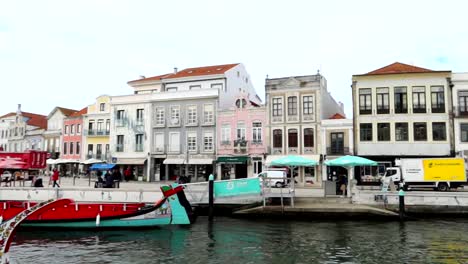 Toma-Panorámica-Hacia-La-Izquierda-Capturando-Barcos-Moliceiro-Frente-A-Edificios-Tradicionales-A-Lo-Largo-De-Un-Canal-En-Aveiro,-Portugal.