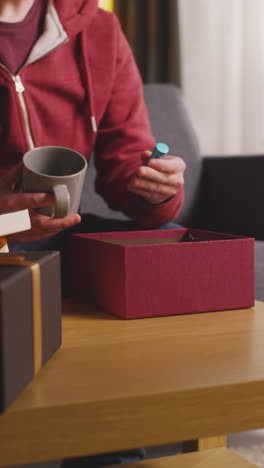 vertical video of man putting present into gift wrapped box decorated with ribbon on table in lounge