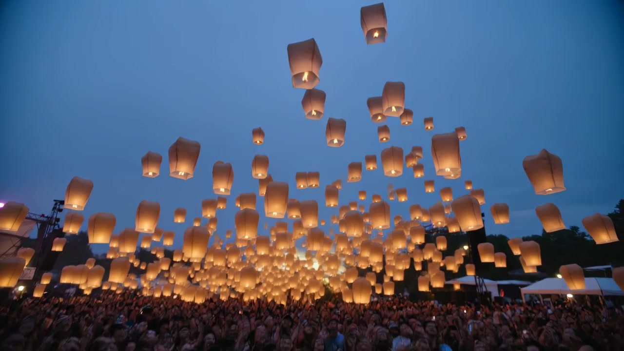 Grupo con ropa de verano encendiendo y soltando linternas de papel brillantes en un parque, celebrando.