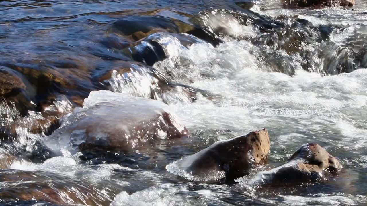 Corredeiras de rio fluindo ao redor de rochas cobertas de gelo no início da primavera