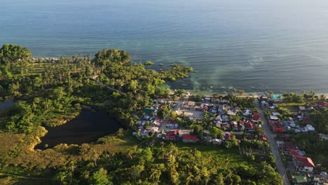 Picturesque aerial drone shot of a coastal village town community with homes amid lush foliage and calm ocean waters - Yocti, Catanduanes, Philippines
