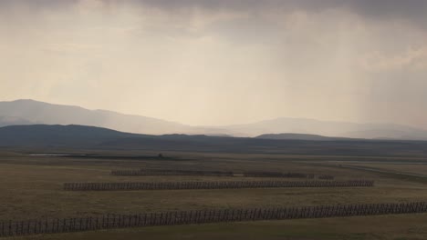 snow fences stretching across a wide open plain under a cloudy sky with distant mountains