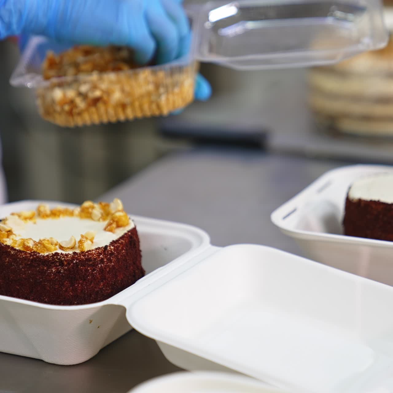 Chocolate cake in individual box being decorated. Gloved hand puts peanuts on top of the dessert. Blurred backdrop