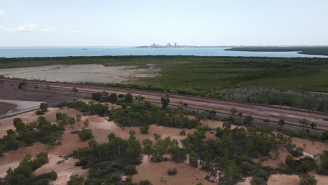 toma aérea ascendente de movimiento lento con drones del área industrial del brazo este y vías de tren con el horizonte de darwin, territorio del norte