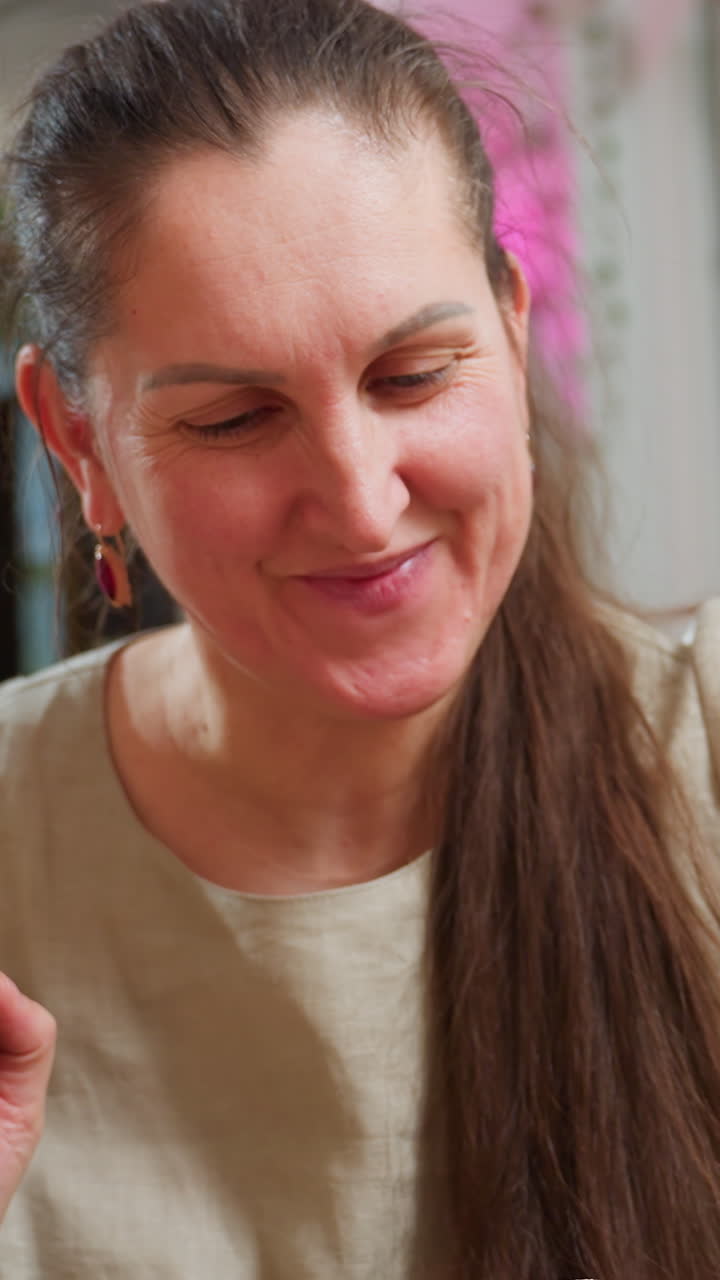 caucasian woman assembling colorful craft mobile with beads and wires, smiling while using hands and pliers, bright playful studio with pink lighting and bunting, DIY ornament scene, joyful hobby