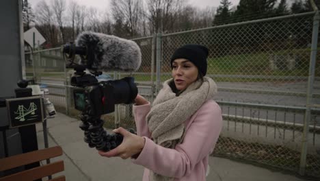 a woman in winter outfit recording a video with her handheld camera at the park in coaticook, quebec, canada - medium shot, slow motion