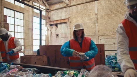 a trio of workers at a waste recycling plant people in uniform sort through plastic bottles according to color during recycling at the plant