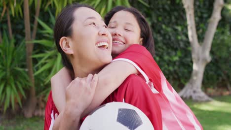 video of happy asian mother and daughter in soccer shirts embracing in garden