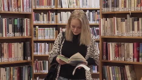 smiling girl is walking towards camera in library between bookshelves