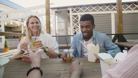 friends chatting and laughing together, while sitting around an outdoor table, eating street food and drinking cold drinks