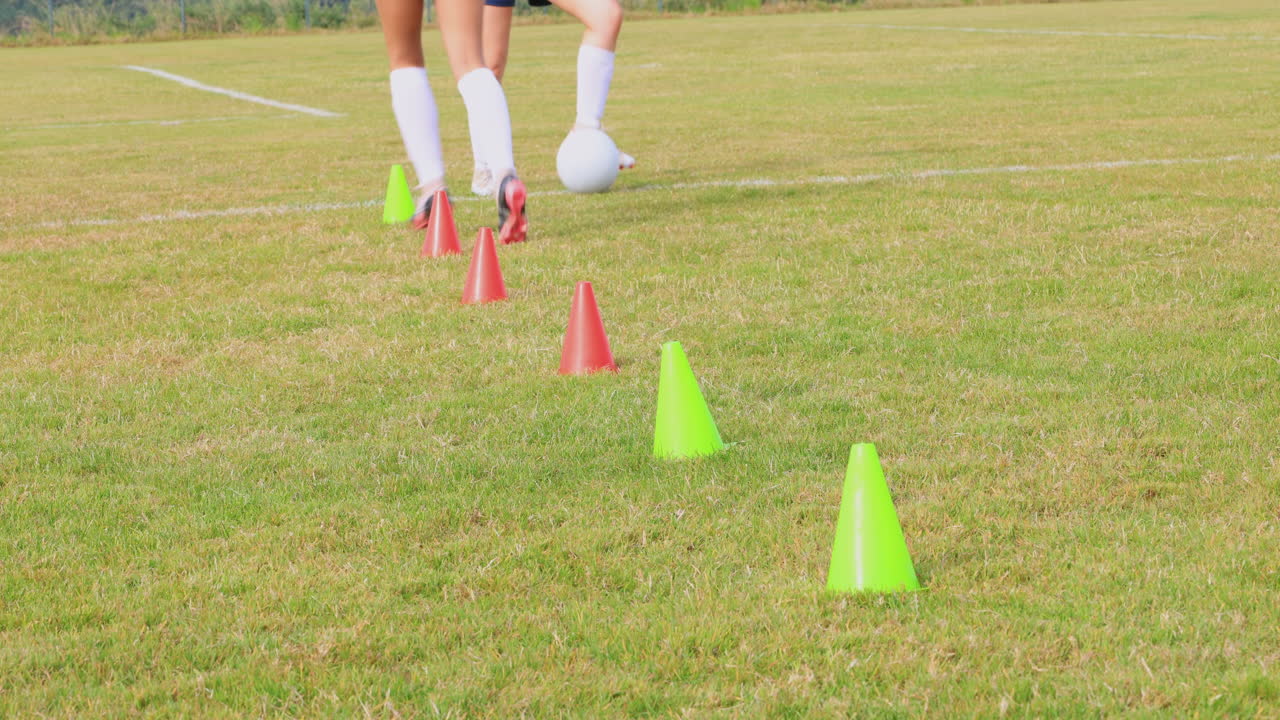 Giocatrici di calcio che indossano pettorine nere, corrono dietro al pallone ed evitano gli ostacoli in campo.