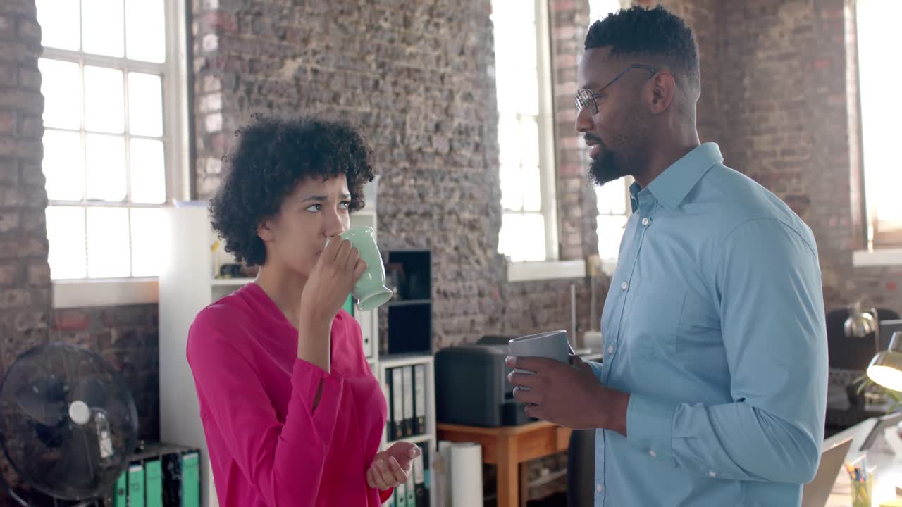 Happy diverse colleagues discussing work and drinking coffee in office in slow motion