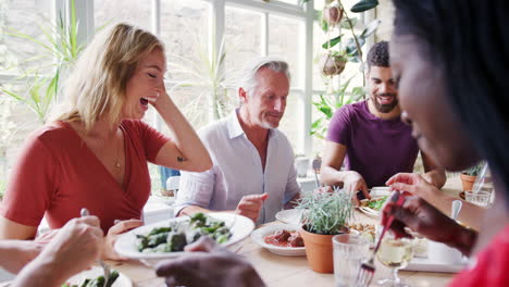 a mixed age group of adult friends eating together at a table in a small restaurant, selective focus