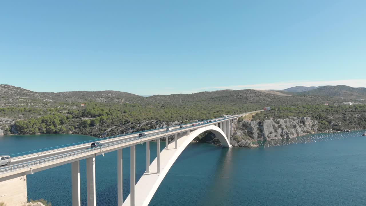 Drone fly over a suspension highway bridge with traffic cars over the Adriatic sea with natural mountain landscape
