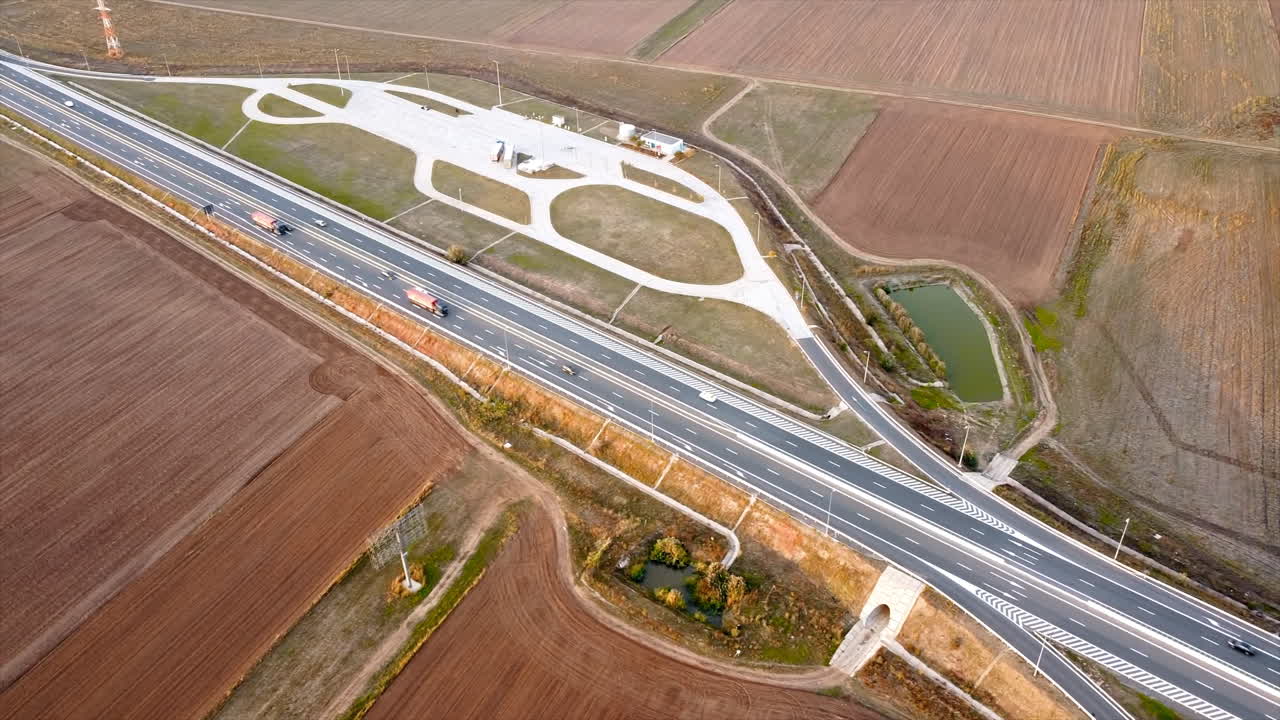 The Motorway of the Sun with moving cars and parking on the side of the road, fields around. View from the drone. Romania
