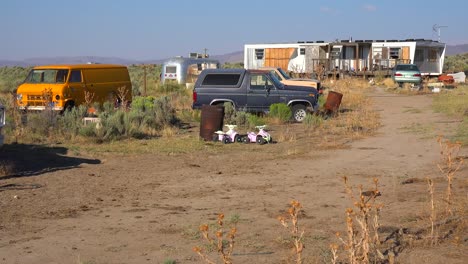 an abandoned mobile home in the desert is surrounded by old trucks and cars and trash 1