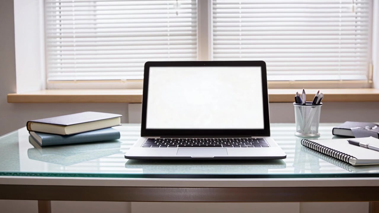 Panoramica a destra, un uomo adulto con una camicia chiara si allontana, rivelando un ufficio domestico con un laptop al centro.