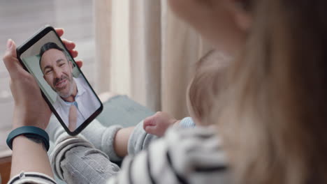 madre joven y bebé chateando por video con el padre usando un teléfono inteligente saludando a la hija pequeña disfrutando de la conexión familiar