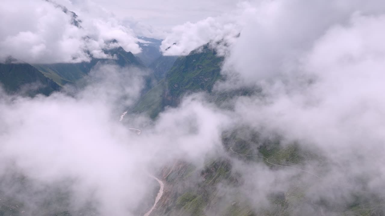 A cinematic drone shot soaring through dense clouds, revealing the Colca Valley with its winding river in the background, framed by dramatic cloud cover.