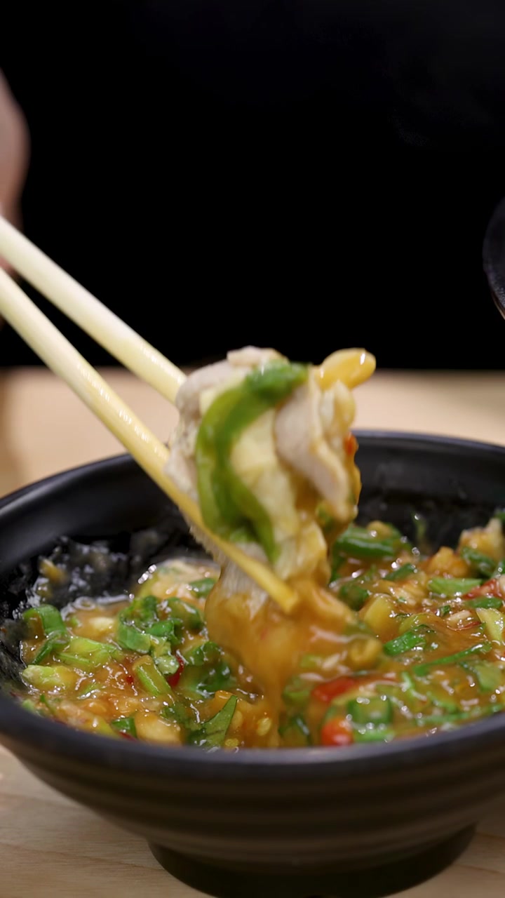 Plano detalhe: pauzinhos levantam frango fatiado e vegetais de uma tigela fumegante de sopa de macarrão asiática picante.