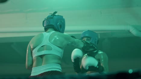 two female boxers in helmets and boxing gloves fighting in ring at gym