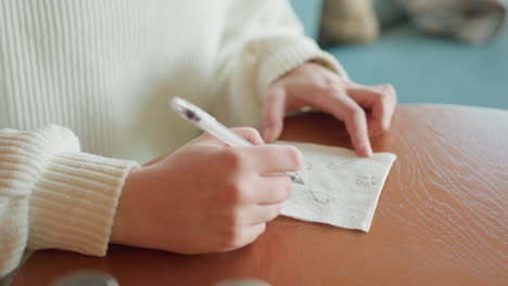 close up of artist hand sketching casual doodles on tissue paper at wooden table, soft daylight and indoor ambiance create cozy atmosphere suggesting creativity