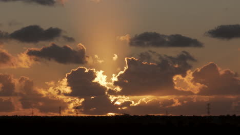 static wide shot of gigantic golden sunset lights shining behind moving clouds silhouette at horizon